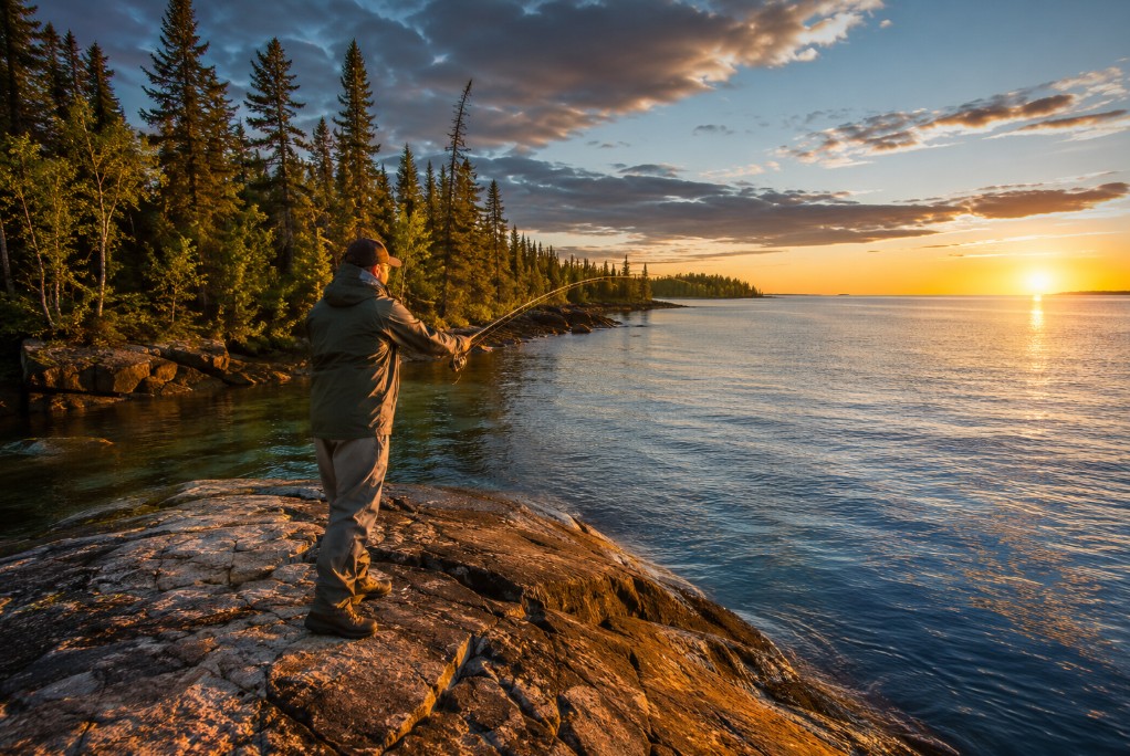 Angler casting from a granite point into clear Lake Superior water near Wawa at golden hour